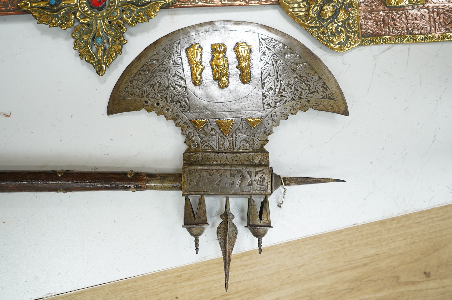 A decorative Indian axe, the large head inlaid with brass Hindu figures, together with a brass mounted North Indian kukri, another similar knife with bone handle, and a large shovel-shaped copper and brass item possibly